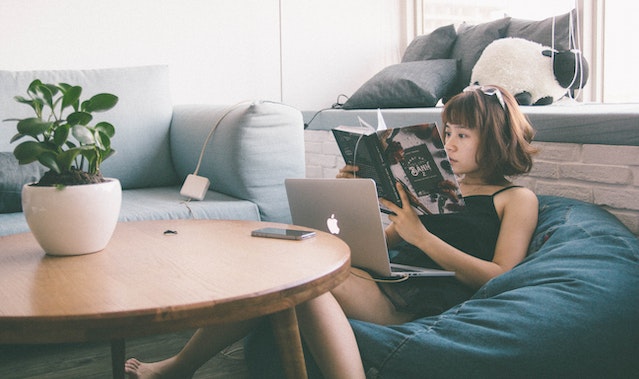 someone reading a book in front of a laptop in a bean bag chair